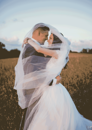 bride and groom cuddling each-other on a flowery field with a touch of wind 